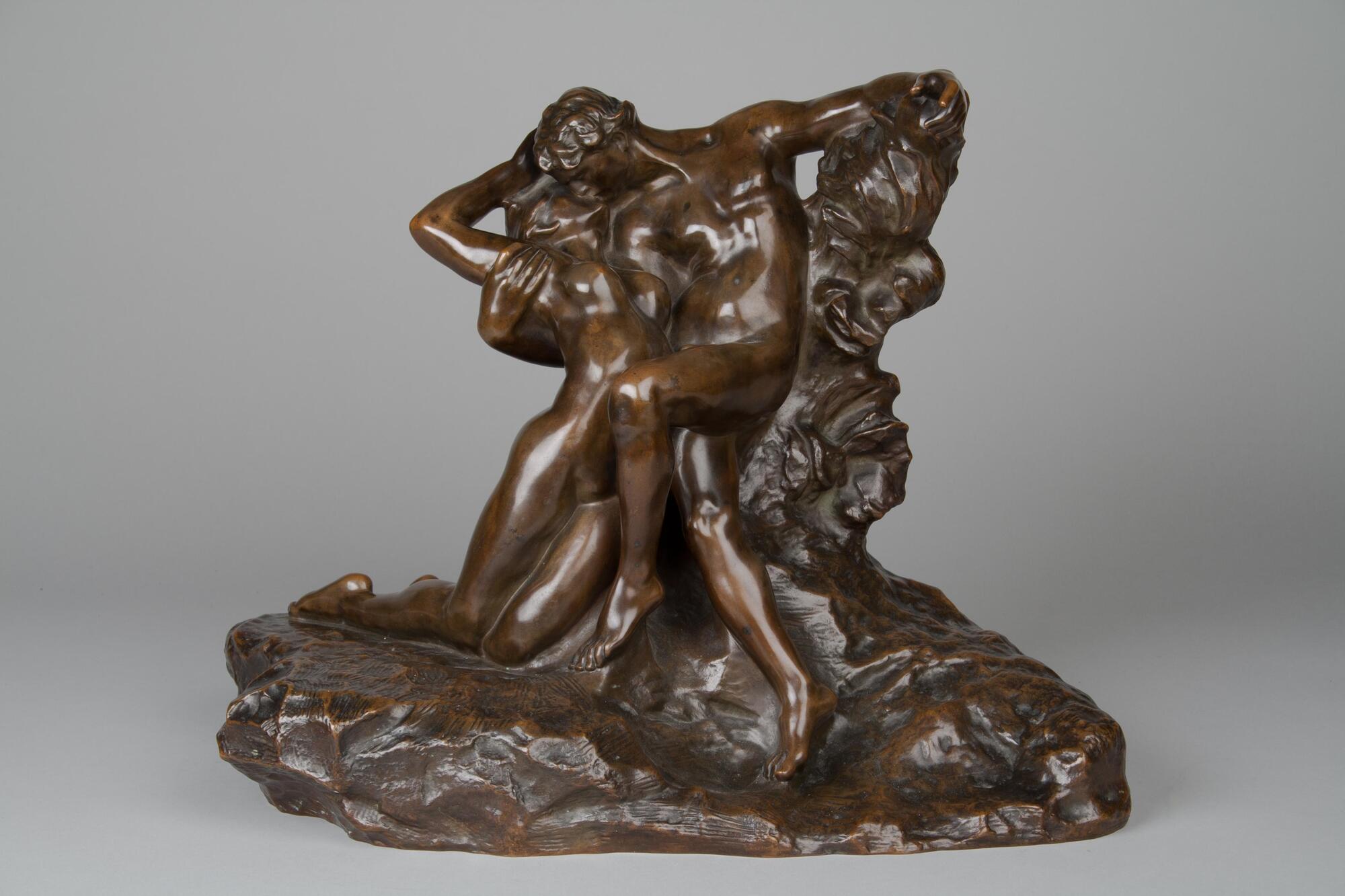 Two nude figures embrace and kiss. The man is seated with his legs crossed as he bends to the side to embrace the woman, his arm under her shoulders. The woman, kneeling beside the man, arches upward and backwards to meet the bending figure of the man. The smooth modeling of the figures is contrasted by the more agitated modeling of the base and the support on which the man sits.