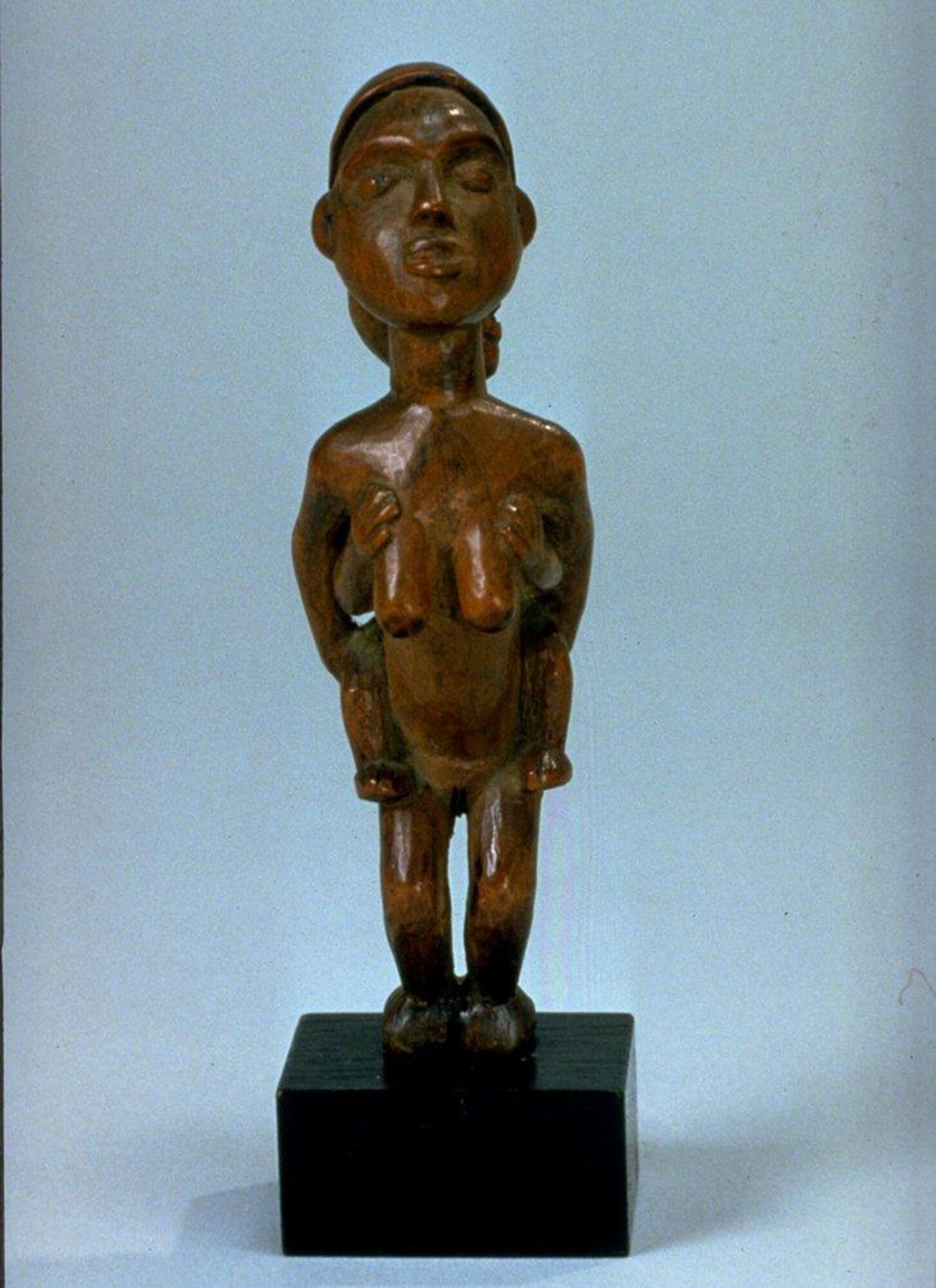 Carved wooden object depicting a female figure with flexed knees carrying a child on her back.