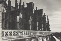 Black and white photograph of the upper floor of a cathedral. The windows are arched and outside of the windows are carved stone barriers.