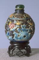 A clay snuff bottle carved with patterned holes and the flowers. On the top is a green glass stopper.