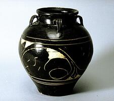 A stoneware jar with a globular shoulder and belly, a tapered base, a short wide neck with flaring rim, and four strap handles connecting the neck to the shoulder.  It is covered in a white slip then a black slip, with sgraffiato floral decoration that cuts through the layer of dark slip to reveal the white slip between bands around the body, covered in a clear glaze. 