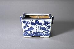 Blue and white square incense burner with a painting of a dragon, clouds, waves, and an inscription.