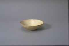 This thin porcelain conical bowl with direct rim on a footring has an interior with molded impressed floral meander and <em>fenghuang</em> 鳳凰 or phoenix decoration. It is covered in a white glaze with bluish tinge, and it has an unglazed rim.