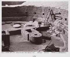 This photograph depicts a view looking down into an ancient stone structure's foundation. An excavation into one of its walls is in progress, revealing the fender of a car.