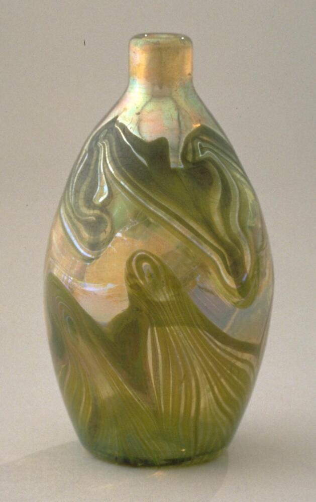 This small bottle consists of iridescent glass with mirror-like surfaces and swirling desigsn in green and brown that evoke agate. The dark designs are in bands that grow up from the base and along the shoulder.