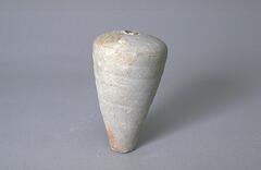 A loosely wheel-thrown, gray stoneware, unglazed vase of <em>meiping</em> (梅瓶) form, tall and tapered, with coarse inclusions. The vase has wide shoulders and a narrow mouth with a small neck. Uneven contour and visible throwing lines leave a ribbed surface, showing kiln effects. 