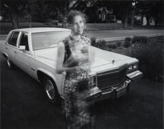 A blurry girl in a dress standing in front of a white Cadillac. She is smiling.
