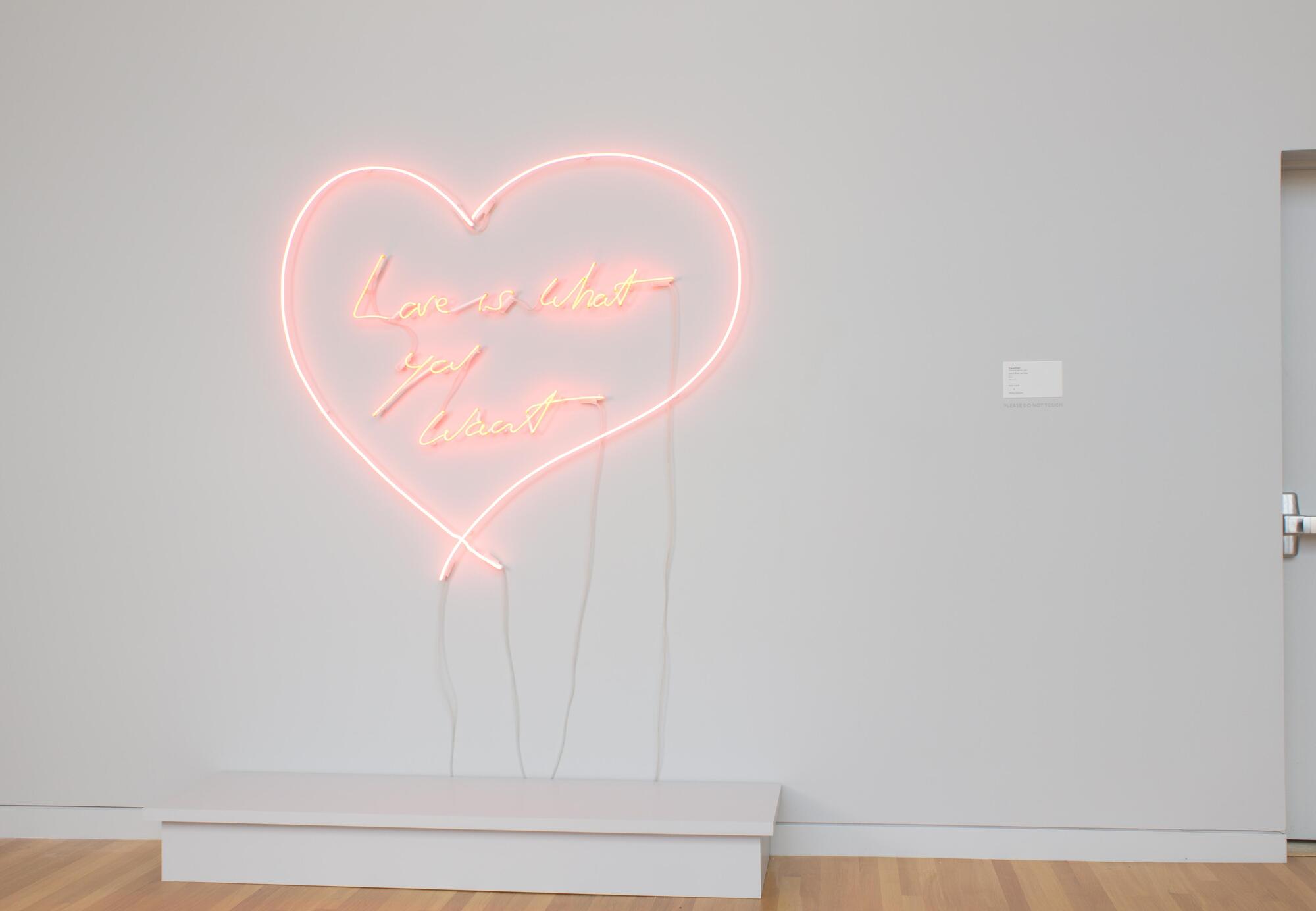 This sculpture is a pink neon light in the shape of a heart with the words &quot;Love is What You Want&quot; inscribed within the heart.