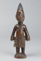 Standing figure on a round base with a square carved on bottom of base. The figure is wearing a cloth around the waist with a diamond pattern and is holding a string with cowrie shells. The hair is tall, in a round comb-like shape. 