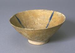 This Kashan style bowl comes from the Seljuk period in Iran. The bowl features a simplified  design of thin cobalt blue stripes that radiate from the interior foot to the rim. The overall bowl is done on a tan ground with a slightly green coloring. The bowl is either late 12th or early 13th century Seljuk pottery.<br />
 