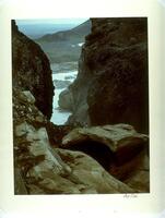 This photograph depicts a view looking down through a rocky passage to a mountainous landscape beyond.