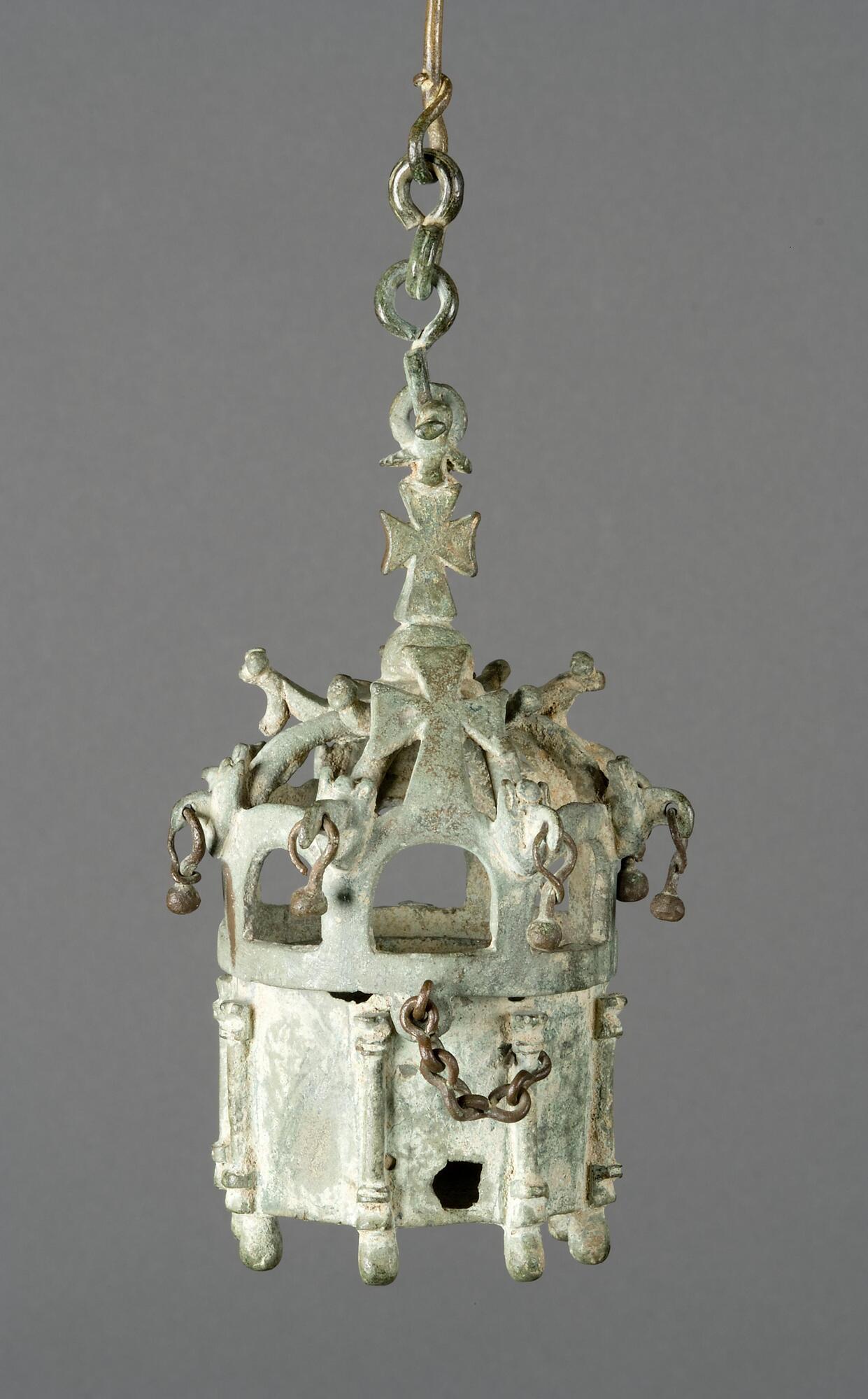 The body of this cylindrical censer is decorated with eight columns spaced at regular intervals. The lid of the censer consists of an openwork dome divided into sections by eight vertical ribs that converge at its apex. An arched horizontal band intersects the midpoint of the ribs, and these eight junctures are marked with a projecting bird that holds a small bronze ball dangling from its beak. Two segments of the dome are decorated with Maltese crosses while another two feature curved plant forms. The apex is surmounted by a finial comprised of a globe topped by a Maltese cross on which a bird holding a piece of fruit perches.