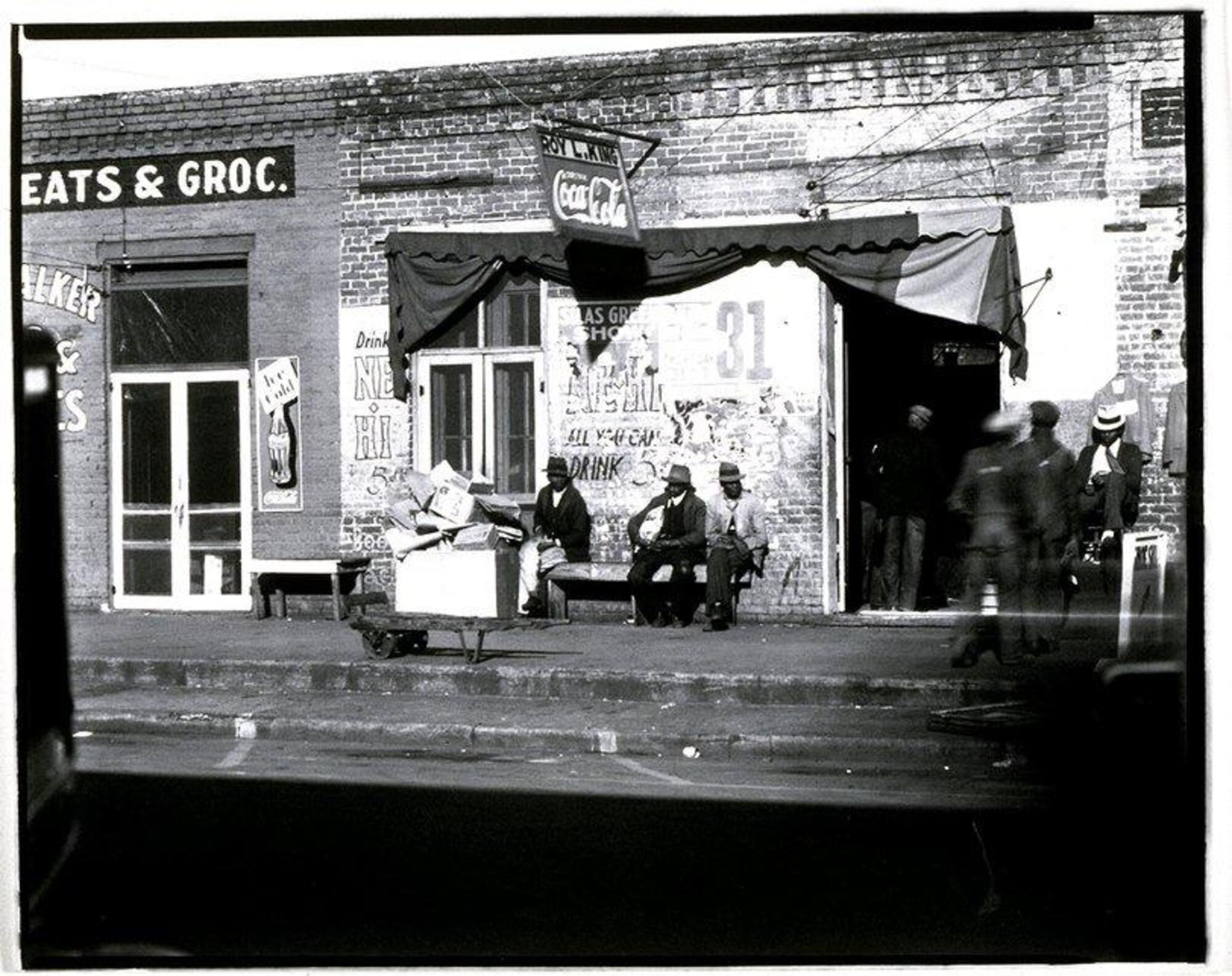 View of a storefront with people sitting in front on benches and entering the shop through a doorway.