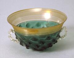 Glass bowl or cup-like vessel with green body, gold striated rim and clear glass handles.