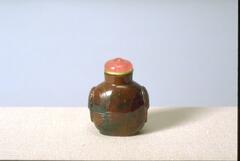 A bloodstone snuff bottle with (taotie masks?) on the side. On the top is a rose colored glass stopper on a green tinted ivory collar.