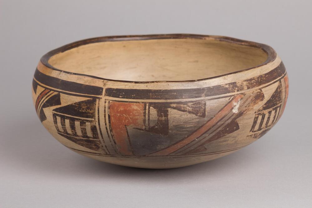 Shallow, tan, stoneware bowl with patterns in shades of black and reddish brown on the exterior. 