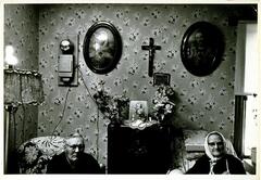 Portrait of an elderly couple in a living room adorned with religious icons.