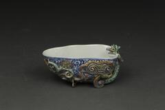 A rounded triangular shaped libation cup with blue underglaze and green and orange overglaze designs on the side and a Qilin on edge.&nbsp;