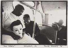 Three people on a bus, all African-American, two women and one man. The two women are talking and one is holding a mannequin head in her lap.