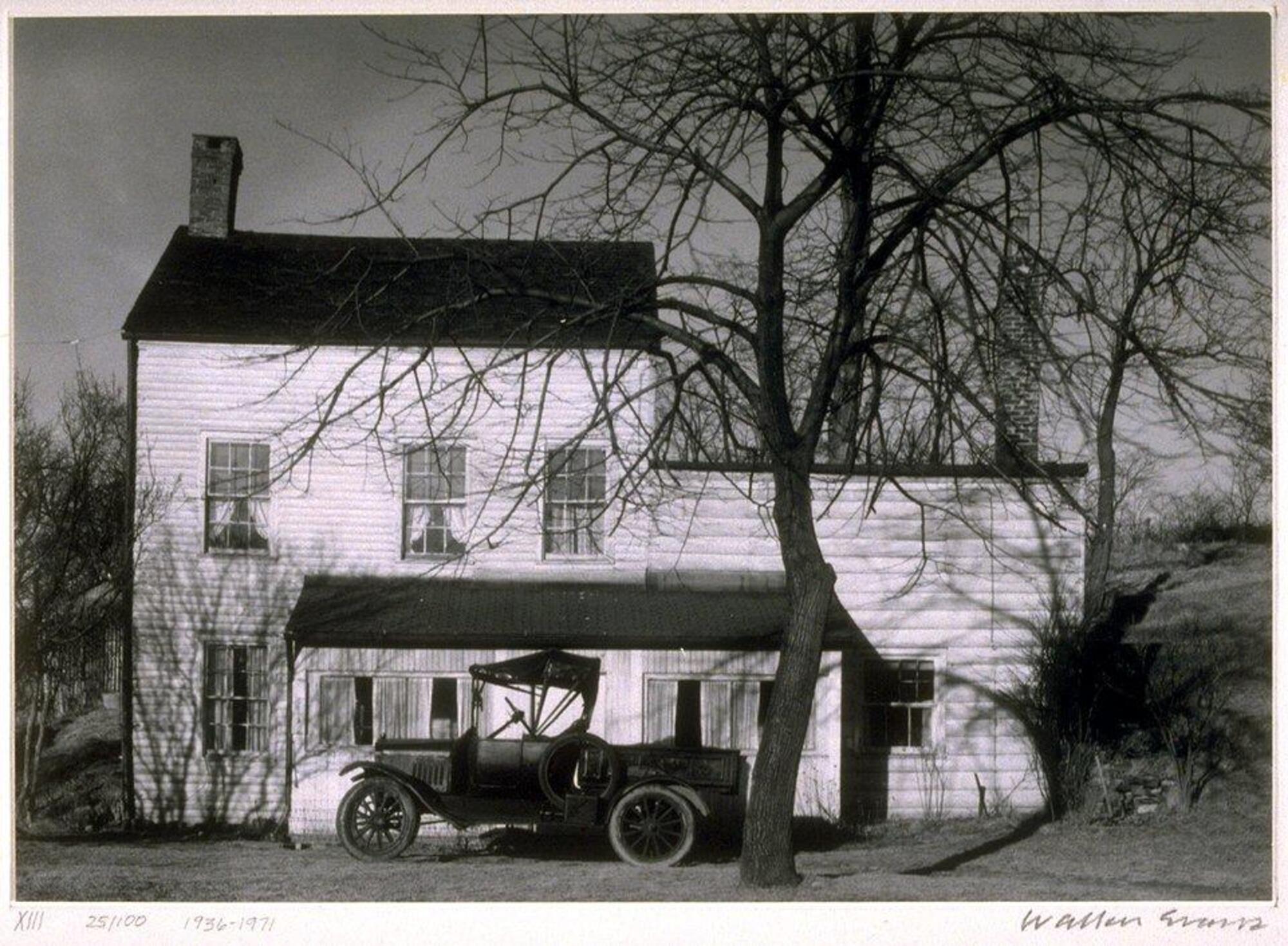 A profile view of a farmhouse featuring a car and a tree without leaves.