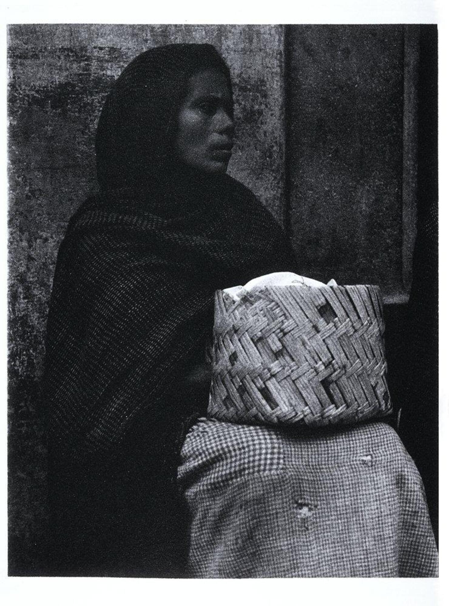 This is a photograph of a woman in Patzcuaro, Mexico. The woman sits with a headscarf draped over her head and shoulders and a basket on her lap.