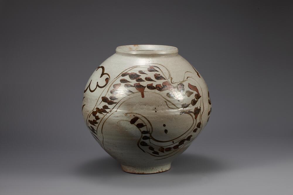 Round porcelain jar with iron pigment under colorless glaze. An abstract dragon spirals around and up the body of the piece, marked by quick brushstrokes indicating scales and unrestrained swirls indicating features such as its head and feet. A slight valley in the contour of the jar marks where two separately thrown pieces were joined together.<br />
The foot is rather small for the size of the body.<br />
<br />
This is a white porcelain jar decorated with iron-painted dragon, which wraps around the jar three times, displaying dynamic strokes of brush. The dragon&rsquo;s head is not rendered; its two eyes have been tersely painted instead. Jars with iron painted dragons, rendered in an abstract from, were produced in large quantities in the 17th century; many of them were produed in regional kilns. Despite slight damage to its rim, this jar is preserved as intact. The central part of its body clearly shows that this jar was created by joining separately produced upper and lower halves.<br />
[Korean Col