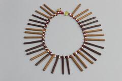 Beaded necklace made up of long dark and light cylindrical wooden beads separated by small white and red beads. Loop and button closure with two large translucent beads.