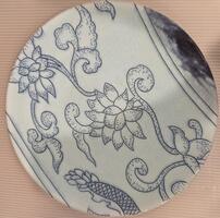 This plate is situated on the border of the piece and depicts blue flowers and vines on a white background. The upper right of the plate is dark blue and blurred.&nbsp;