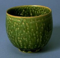 A finely potted deep stoneware beaker with a rounded bottom and a mottled, dark green glaze. The attractive glaze effect is achieved by applying small dots of a wax over the entire surface of the vessel, and then pouring the glaze from the top down. Unglazed ring interior is the result from a clay ring to separate one pot from another in firing.