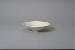 A thin conical porcelain bowl with a direct rim on a footring and an interior with incised cloud-like decoration. It is covered in a white glaze with bluish tinge.