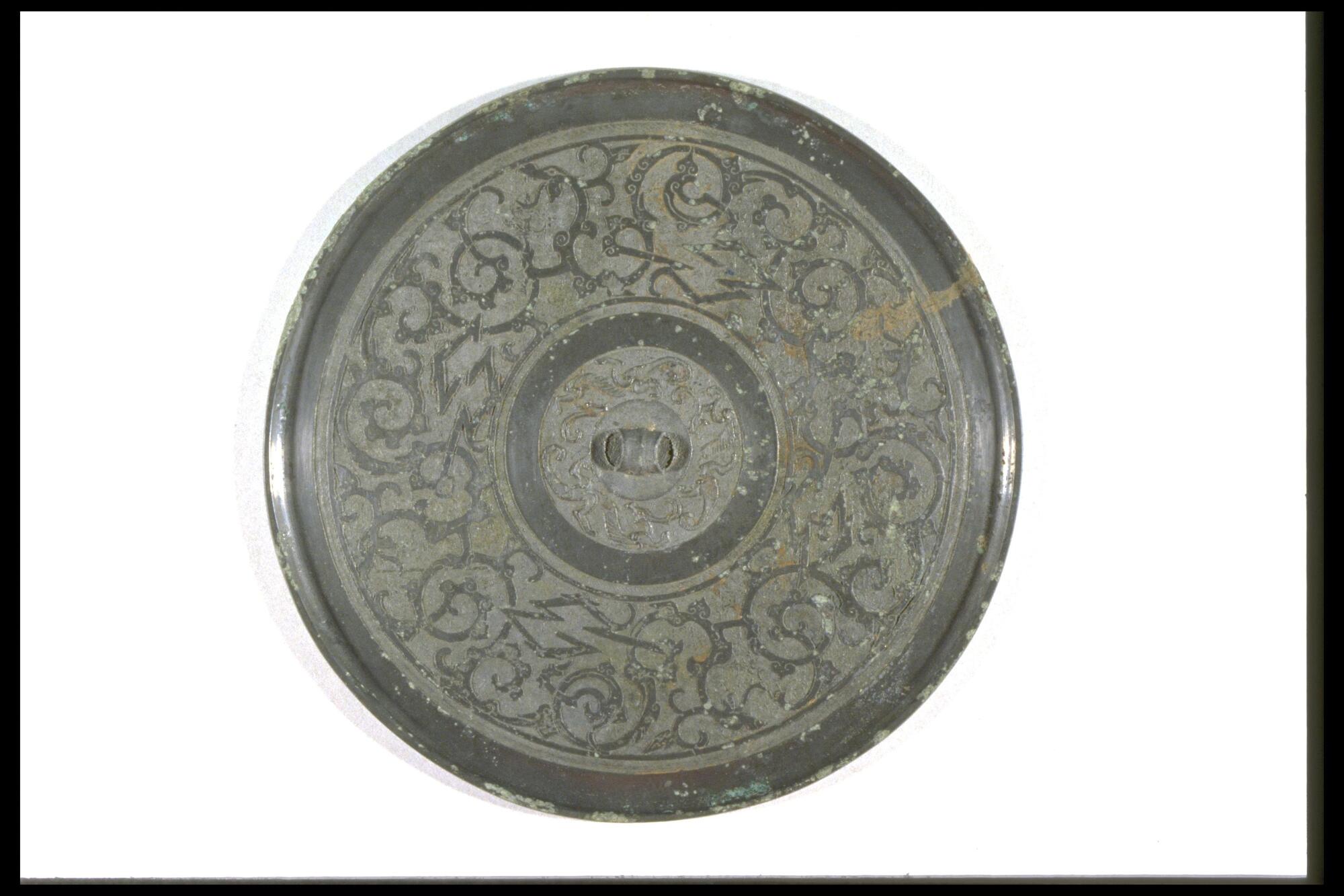Thinnly cast mirror with narrow rim and bridge-shaped knob, back decorated with interlaces of serpentine and angular meaders, front side polished flat