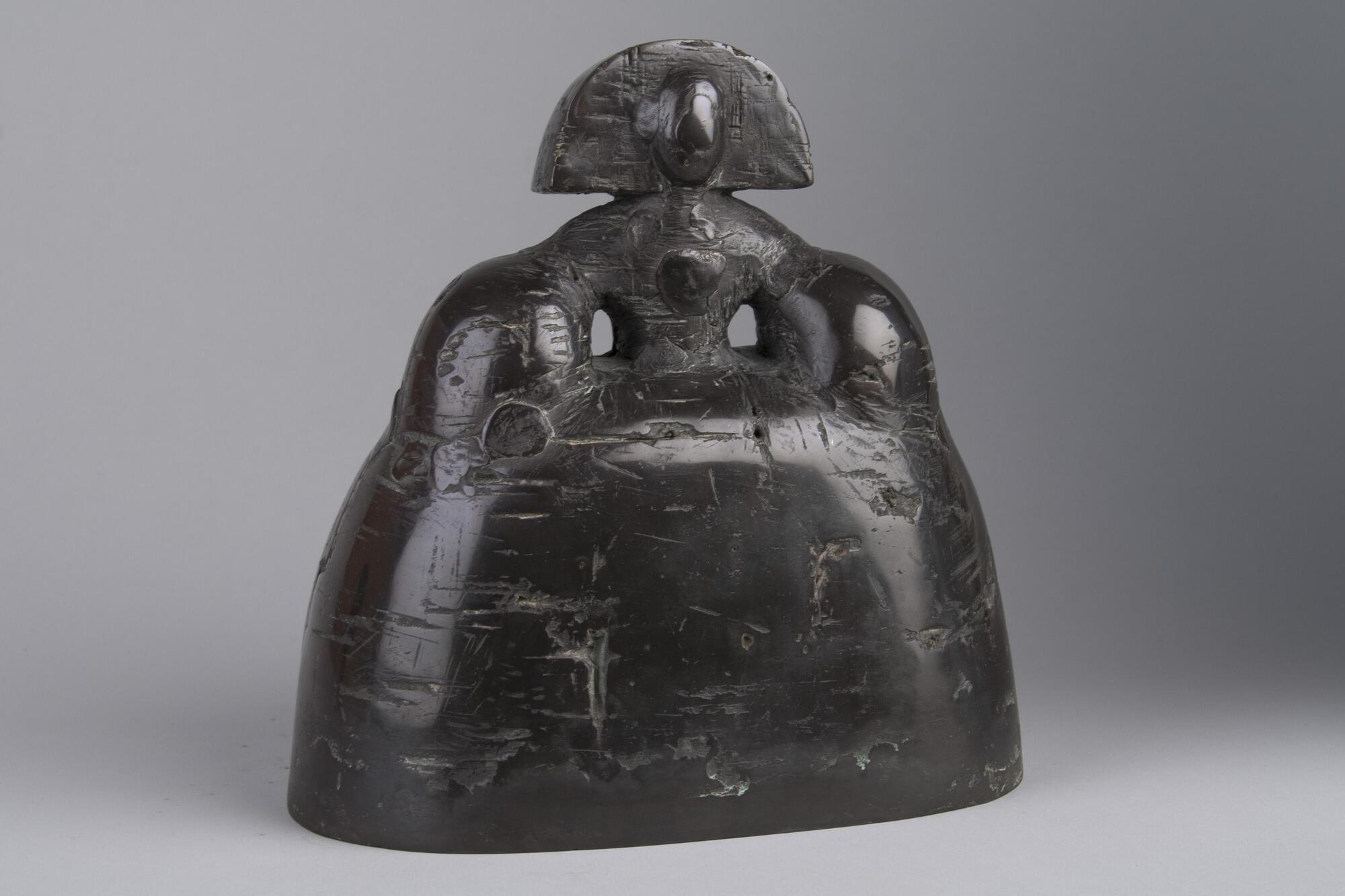 A bronze figure of a girl. The bottom half is a bell shaped skirt white the top half is of a girl wearing a hat that ends at her shoulders.