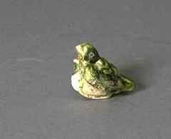 A ceramic funerary sculpture in the shape of a small green sitting bird.