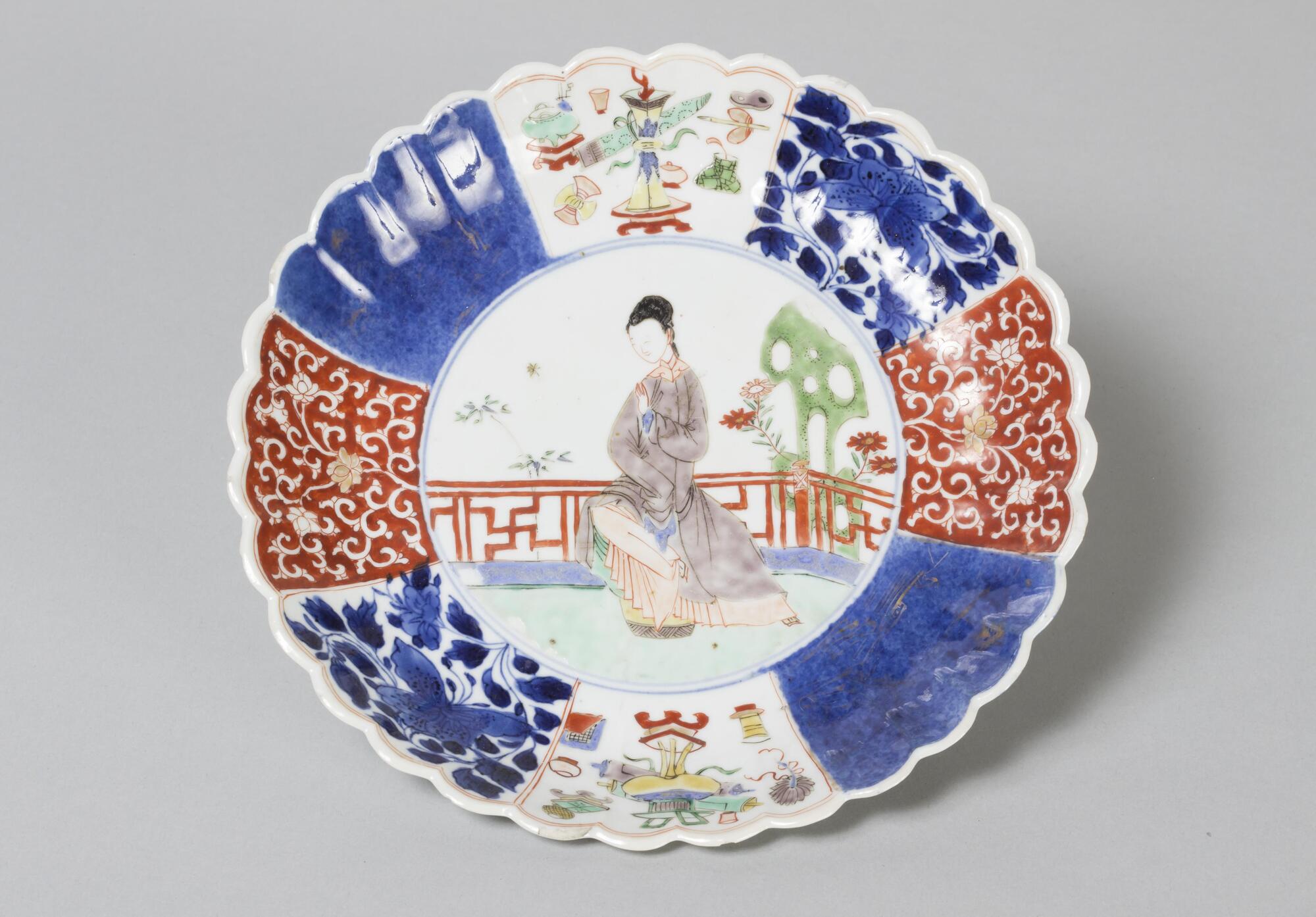 A scalloped plate with design of a lady in the center, wearing a grey dress in a garden.