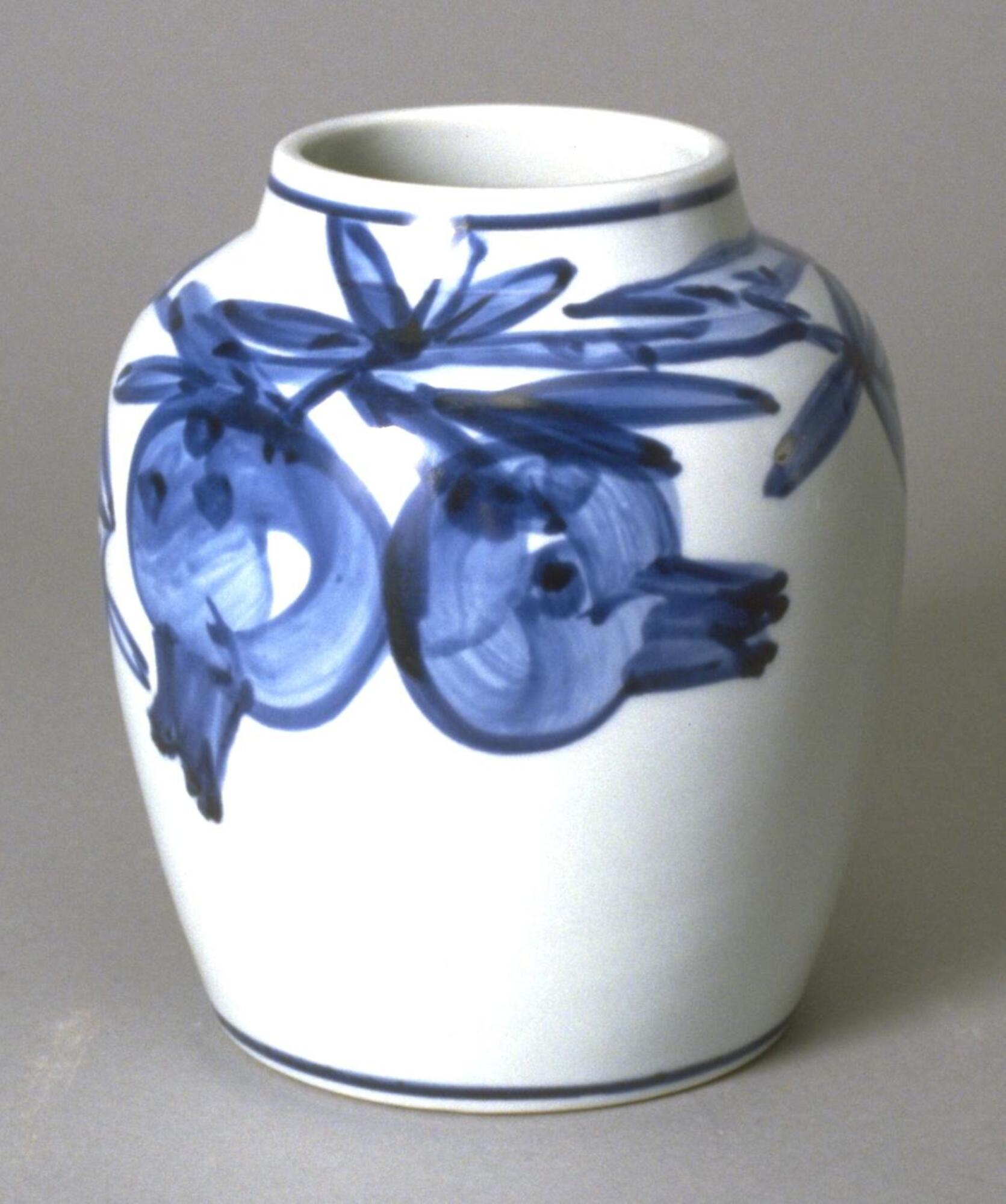 It is a medium size porcelain vase with pomegranate design in blue underglaze. The body is round with gentle shoulders; the mouth is wide and the neck is short and slightly inward. It has no foot. The pomegranate fruit and leaves are quickly executed with broad brush around the shoulder and the middle of the body. There is a band of a single line around the mouth and another around near the bottom. There is the artist’s signature “yû” on the eye. There is no foot but unglazed ring around the bottom; the eye is glazed.
