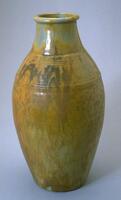 This ceramic vase has a long oval shape with a wide neck, rounded lip and sloping shoulder area. The circular rings from the process of being thrown on the wheel can be seen beneath the glaze. The glaze is a yellow-orange matt, with dark brown patches, over a shiny celadon green and iridescent purple base.