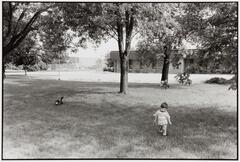 A little boy and a dog in a field with a low-level brick building in the background.