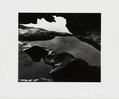 A black-and-white image of pools of water among mounds of wet sand.  A fragmented white sky creates an abstract background.  