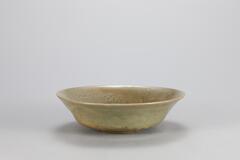 <p>The inner base and walls of this celadon dish are mold-impressed with a peony and peony scrolls, respectively. The low foot retains traces of quartzite supports in three places. The glaze is poorly fused, showing traces of its running, while partial oxidization has given the dish a yellow-green hue in parts.<br />
[<em>Korean Collection, University of Michigan Museum of Art </em>(2014) p.114]</p>
The rim of this celadon saucer is outward flared. Fine crackles are present throughout the surface of the saucer, coated with a dark bluish green glaze. It has glazed short foot with 3 spur marks and is molded peony design on wall and bottom. The exterior glaze color change due to over heating, fired in sagger that was not tightly closed.