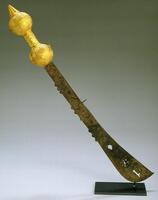 This sword has an iron blade that is narrow toward the handle and gradually widens at the top, ending in a slight curve. Along the edge of the blade are small, half-circular knobs and near the top of the blade there are geometric cut-outs. The handle is formed by two spheres connected by a bar. At the bottom of the handle is a conical projection. The handle is covered in gold-leaf.&nbsp;