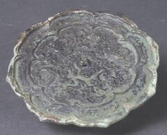 This is an eight-lobed bronze mirror in a dark green or blackish green hue. It is divided into two registers by eightlobed ridge, first of which is decorated with floral scrolls. The inner register has two cranes encircling the suspension loop in the center with their wings extended and facing each other. This object may be compared to other crane-patterned mirrors excavated from the Geumcheon-dong tomb site in Cheongju-si, Chungcheongbuk-do Province.
<p>[Korean Collection, University of Michigan Museum of Art (2017), 241]</p>
