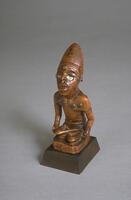 Small, carved male figure, seated atop a block, with legs crossed. The naturalism with which the expressive face is carved, the high crested coiffure (or chiefly cap?) and the progressive foreshortening of the body show the importance given to the head in Yombe aesthetics. The figure's eyes are mirrored glass, and the upper body, face and head are studded with brass tacks. A slight vertical crack can be seen at the figure's sternum.<br />
The Yombe figure was identified for UMMA by Allen Roberts and Mary (Polly) Nooter Roberts. There was a discrepency regarding the dating of the piece: the export paperwork said "circa 1830", but the dealer's catalogue said early 19th c. When asked to help resolve the dating, Polly Nooter Roberts replied: "As for the Yombe figure, I can tell you with certainty that it is NOT early 20th century, and is definitely from the 19th century, if not earlier. I cannot confirm the 1830 date, but I would be more inclined to believe that than the early 20th century. So, I think you can co