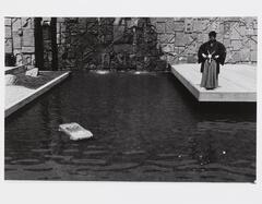 In this photograph, a man stands over a shallow pool, looking at a submerged toy car.