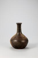 Bottle with a long, narrow neck such as this one was generally used in private homes and restaurants to hold alcoholic drinks. Part of the body has come into direct contact with flames during firing, leaving the glaze scorched and volatilized. Glaze has also boiled and come off in parts of the shoulder. The foot is flat and wide, and clusters of soot have stuck to the lower part of the body. There are throwing marks on the neck and lower part of the body.<br />
[Korean Collection, University of Michigan Museum of Art (2014) p.212]