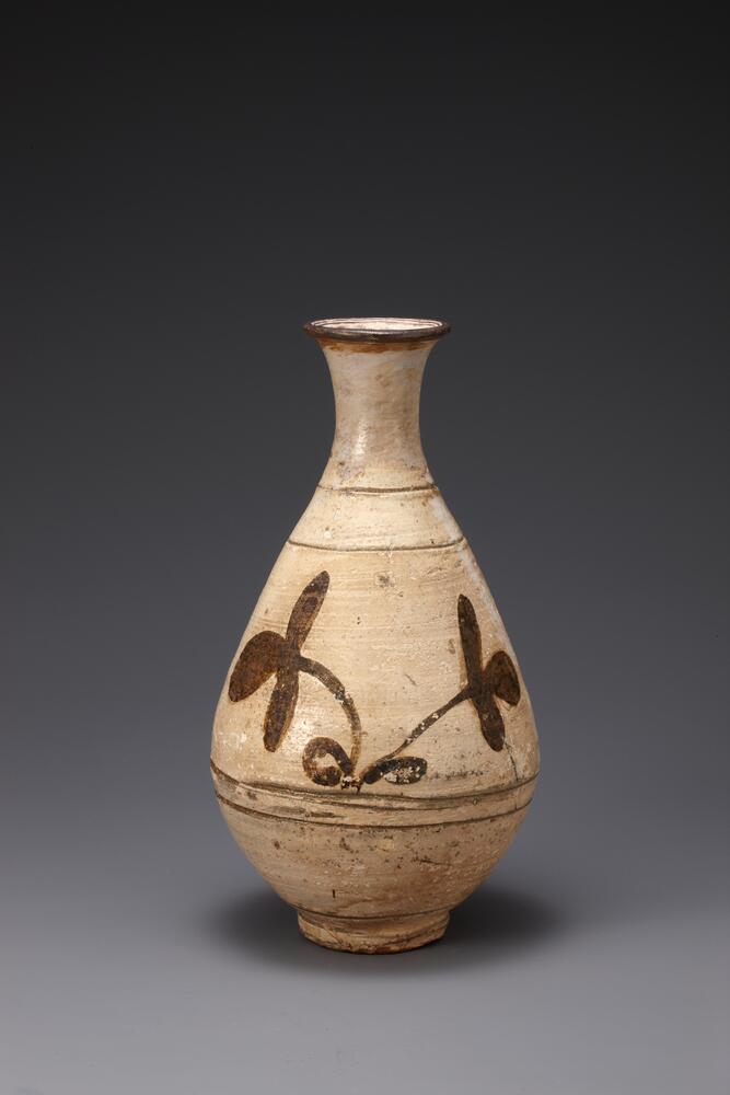 Most buncheong bottles excavated from tombs have damaged mouth. This bottle, too, has been repaired after complete breakage of its rim. The chemicals used during the restoration have flowed down to the center of the body. The rim of the foot reveals the unglazed body and shows the traces of building the foot. The bottle was produced at a kiln in Hakbong-ri, Gongju-gun, Chungcheongnam-do. Its glaze was thinly applied, thus the iron-oxide pigment and white slip have peeled off in many places.<br />
[Korean Collection, University of Michigan Museum of Art (2014) p.153]