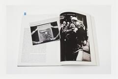 Image of a book lying open to a page featuring a photo of a person being restrained by another person in riot gear. A newsclipping featuring Munch's Scream lies on the book across the open page.  