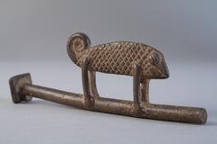 Small brass sculpture of a chameleon, tail is in a swirl, on a brass rod.