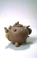 The globular teapot is modelled in the form of a pomegranate applied with fruits and nuts. It has a water-chestnut-form handle and a lotus shoot-form spout that is impressed with two seals. The cover is fashioned as a mushroom. The stoneware is of a speckled beige-brown colour.