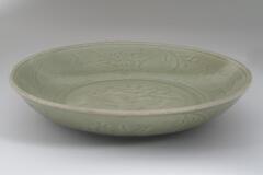 A wide, shallow bowl with curved sides and a direct rim on a footring.  It is incised on the interior and exterior with floral meander.