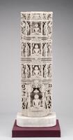 This column fragment consists of a base with a seated jina in the center with a tiered umbrella above him under an elaborate arch flanked by two figures to either side—two male and dancing females at the outside.  Three virtually identical bands above it represent smaller seated jinas in less elaborate pavilions.  A pair of male cauri bearers with a devotional male on the outside flanks each of the two central figures.  The top figure is flanked by the pair of cauri bearers, but with an elephant surmounted by a lion figure on either side.   There is no cognizance present to identify any of the four jinas, all are depicted in lotus position and their hands in dhyana mudra, a meditation gesture.   <br />